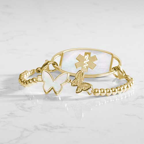 Serenity Stretch medical ID bracelet featuring gold filled beads and adouble butterfly centerpiece adorned with crystal and mother of pearl inlay, attached to a gold medical ID tag featuring mother of pearl inlay and a gold caduceus.