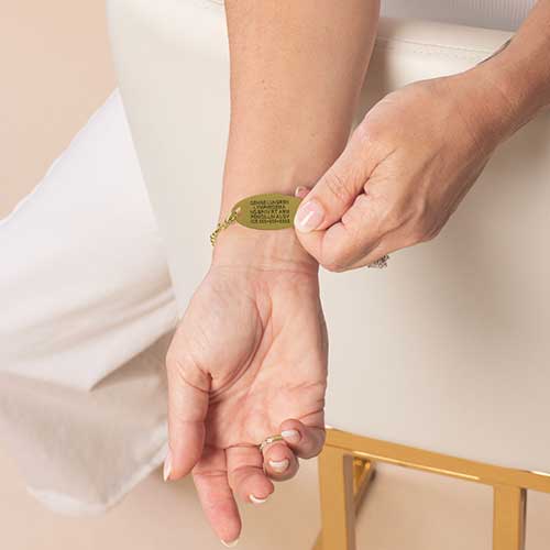 Woman displaying custom laser engraving on her gold toned medical ID tag.