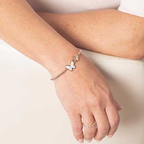 Woman displaying rose gold tone, beaded stretch bracelet with double butterfly centerpiece featuring crystals and mother of pearl inlay.