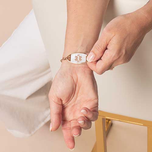 Woman displaying her rose gold toned medical ID tag, featuring inlaid mother of pearl and a a rose gold caduceus.