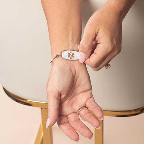Woman displaying her rose gold toned medical ID tag, featuring inlaid mother of pearl and a a rose gold caduceus.