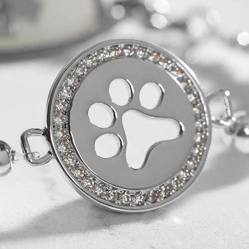 Close-up of the paw print charm on a silver beaded medical alert bracelet, highlighting the crystal detailing around the cutout paw shape.