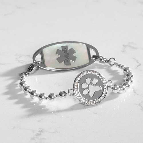 Silver beaded stretch medical alert bracelet with paw print charm and white MOP ID tag, displayed on a white marble surface.