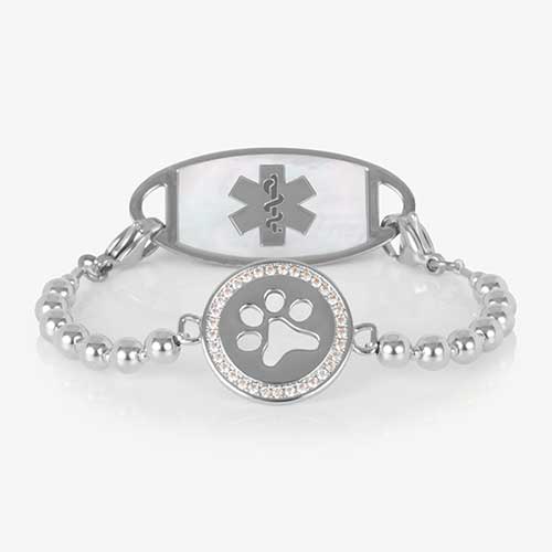 Medical alert bracelet with a silver beaded stretch strand and a round charm featuring a crystal-lined paw print, shown paired with a white mother-of-pearl medical ID tag.