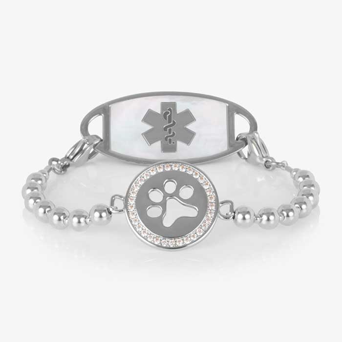 Medical alert bracelet with a silver beaded stretch strand and a round charm featuring a crystal-lined paw print, shown paired with a white mother-of-pearl medical ID tag.