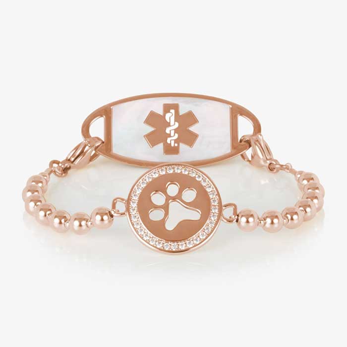 Rose gold beaded medical alert bracelet with a circular centerpiece featuring a cutout paw print and a border of clear crystals, displayed on a white background.