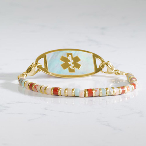 Aris medical ID bracelet in gold featuring flat heishi-style gemstone beads in coral, cream, aqua, and red tones, paired with a gold and white mother-of-pearl ID tag.