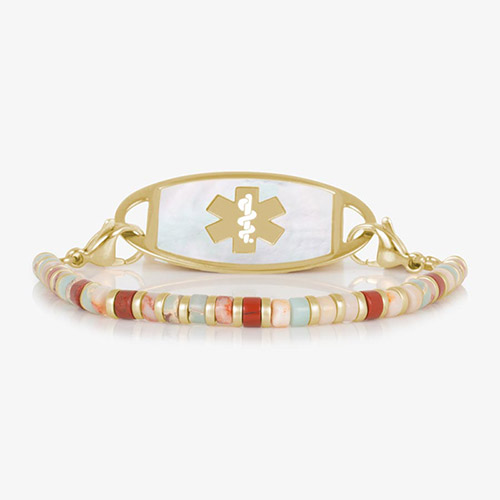 Gold medical ID bracelet featuring a strand of earthy heishi-style beads in shades of red, cream, peach, and aqua, paired with a mother-of-pearl inlay tag engraved with a gold medical symbol.