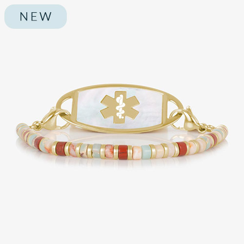 Gold medical ID bracelet featuring a strand of earthy heishi-style beads in shades of red, cream, peach, and aqua, paired with a mother-of-pearl inlay tag engraved with a gold medical symbol.