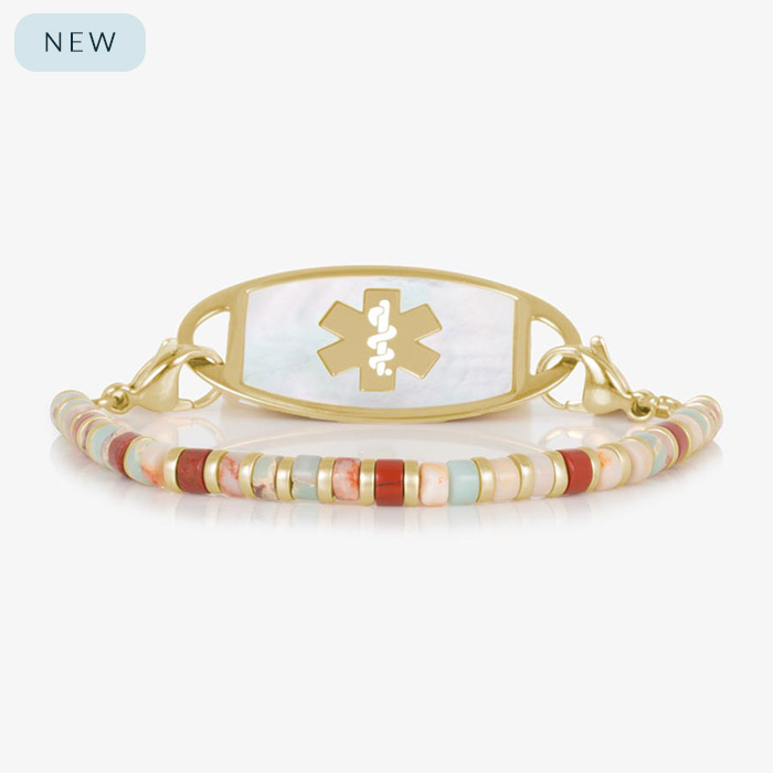 Gold medical ID bracelet featuring a strand of earthy heishi-style beads in shades of red, cream, peach, and aqua, paired with a mother-of-pearl inlay tag engraved with a gold medical symbol.