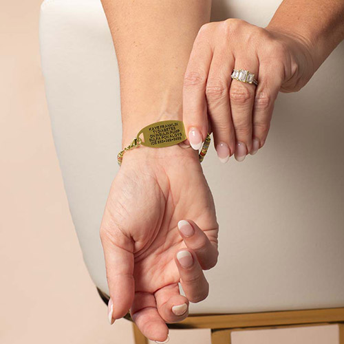 Woman wearing a Lauren’s Hope Aris medical ID bracelet in gold, with personalized engraving visible on the tag, showing colorful heishi-style beads.