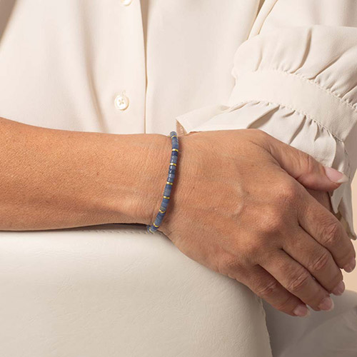 A woman’s wrist wearing the Azores Gold bracelet, emphasizing the slim, vibrant blue and gold beaded strand in a sleek silhouette.