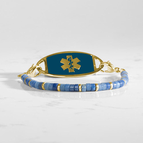 A gold and blue medical ID bracelet with small matte blue rondelle beads and glossy gold-tone accents, attached to a gold-tone tag inset with a bold dark blue panel and engraved medical caduceus.