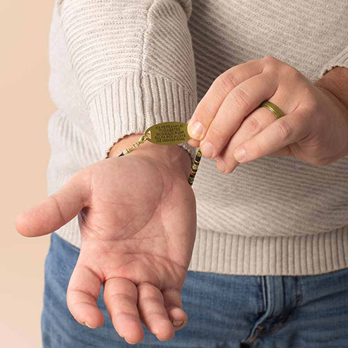 Man wearing a green and gold beaded medical ID bracelet with custom engraving on the gold tag, showing essential emergency information.