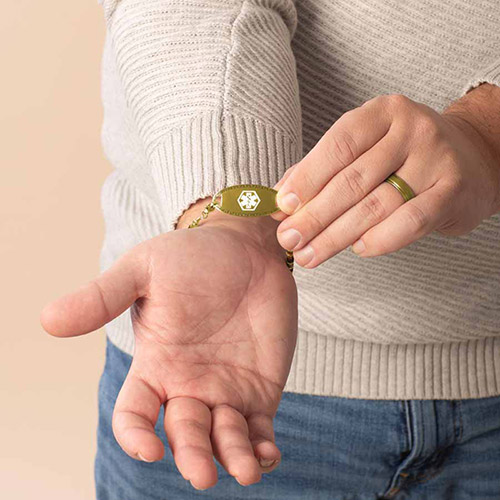 Man displaying the front of his gold medical ID bracelet featuring a white medical symbol, highlighting the bracelet's emergency alert design for men.