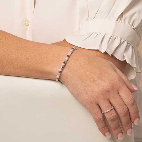 Woman displaying a beaded bracelet featuring gold tone, howlite, and Amethyst beads on a stretch bracelet.
