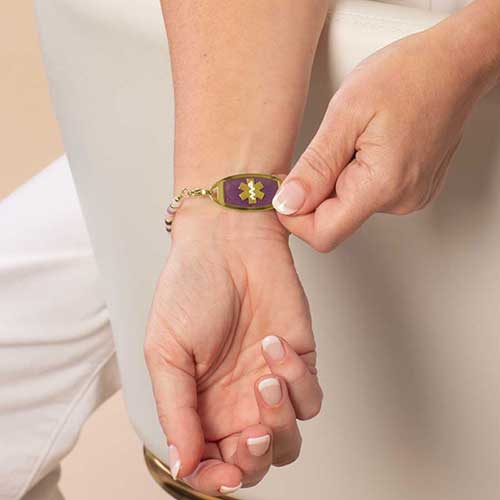 Woman displaying her a gold tone medical ID with Amethyst inlay and gold tone caduceus medical symbol.