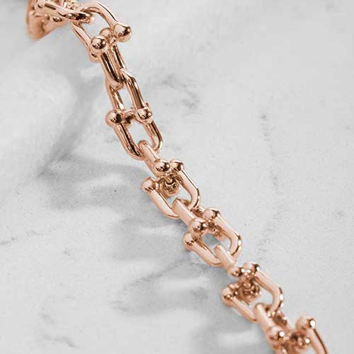 Close-up of polished rose gold-tone links with decorative barbell-style accents.