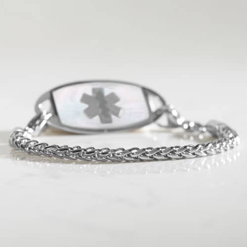 Silver-tone wheat chain medical ID bracelet with mother-of-pearl tag photographed on a reflective surface.