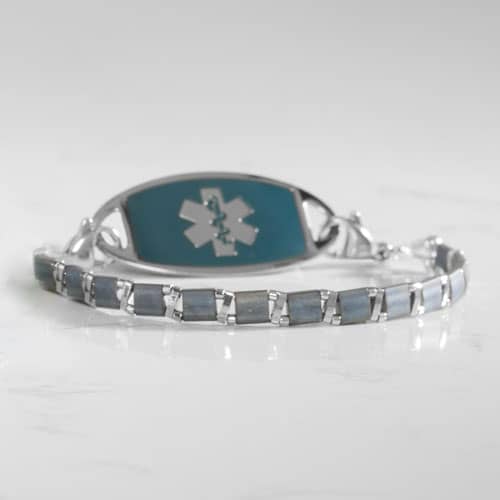 Slate blue tiled bracelet paired with a teal medical ID tag on a white marble surface.