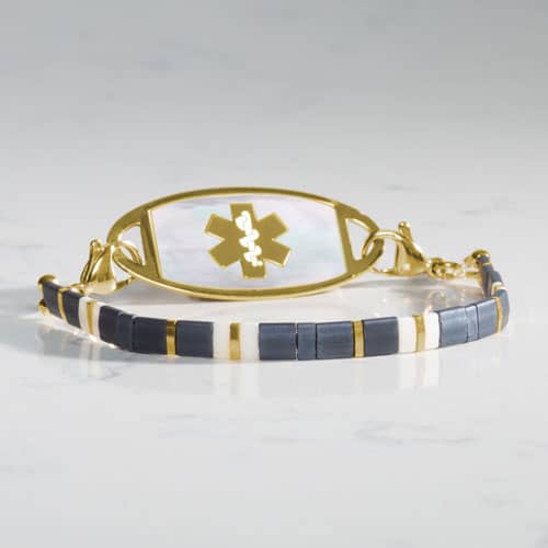 Gold-tone medical ID bracelet featuring a white mother-of-pearl tag with Star of Life and blue, white, and gold tile beads.