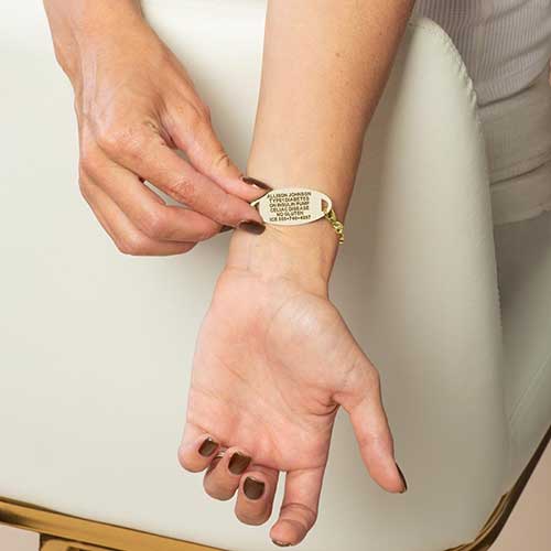 Person displaying the engraved back of a gold Tilly medical ID bracelet on the wrist.