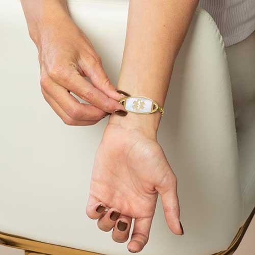 Person displaying the mother-of-pearl Star of Life tag on a gold Tilly medical ID bracelet.