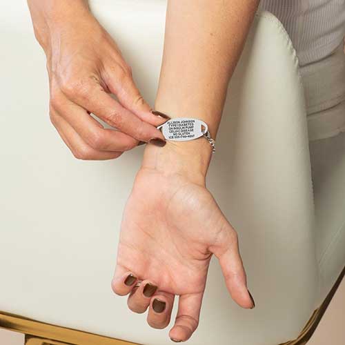 Person displaying the engraved back of a silver medical ID bracelet on the wrist.