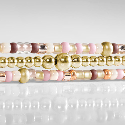 Close-up of the three-strand bracelet highlighting gold-tone beads and pink, cream, brown, clear, and rose-tone accent beads.