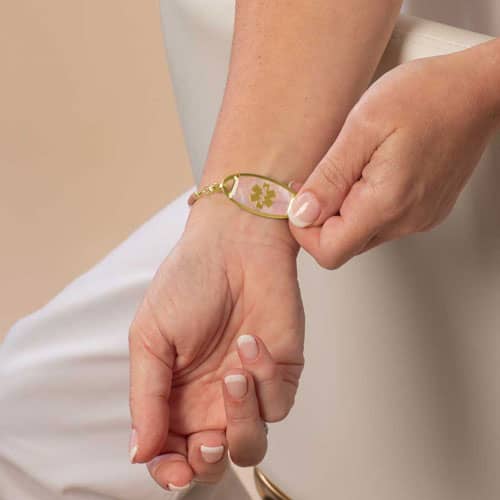 Model is wearing a gold-tone medical ID bracelet while holding the tag to display the white medical symbol.