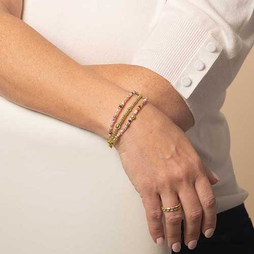 Model wearing a three strand, beaded, medical ID bracelet, featuring gold and blush accents