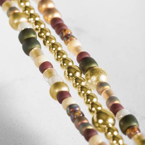Close-up of the bracelet’s three strands featuring gold-tone beads with cream, burgundy, green, and multicolor accents.