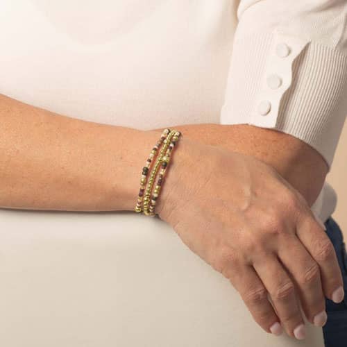 Model is wearing a three-strand bracelet with gold-tone beads and muted cream, burgundy, green, and multicolor accents.