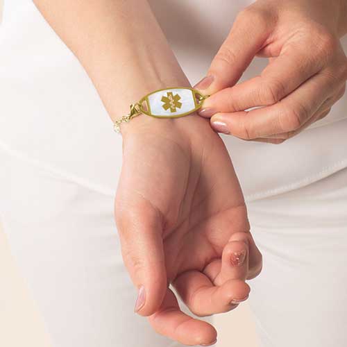 Woman wearing a gold toned mother of pearl inlaid medical ID tag.