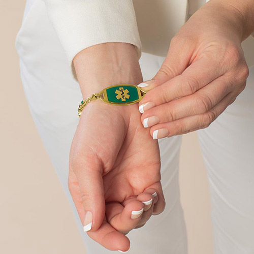 Kate Medical Alert Bracelet in 12k Gold Plate with pear and marquis bezels, shown on wrist, displaying shades of emerald and clear crystals