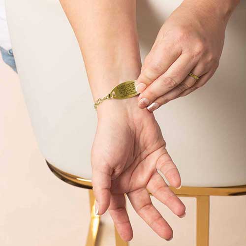 Woman wearing a gold medical ID bracelet with personalized engraving on the back of the tag, featuring 14k gold-plated links and CZ stones.