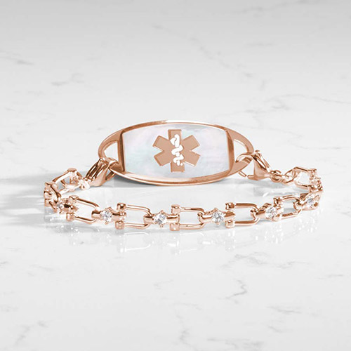 Rose gold women's medical ID bracelet with a mother-of-pearl inlay and rose gold medical caduceus symbol, paired with a CZ-accented link chain, displayed on a marble background.