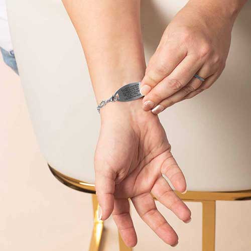 Woman showing the back of a silver medical alert bracelet engraved with emergency information, featuring the Diana CZ chain.