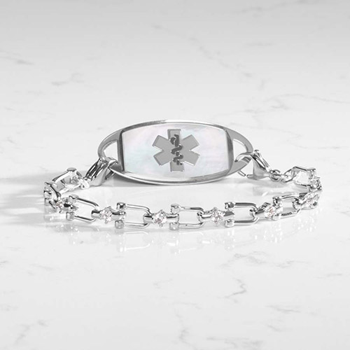 “Lauren’s Hope Diana medical ID bracelet in polished silver with white mother-of-pearl ID tag and CZ-accented chain, displayed on a marble surface.