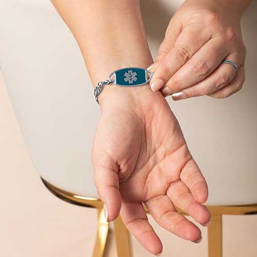 Stylish women’s silver medical ID bracelet with blue crystal accents and a teal medical alert tag, shown on wrist for scale and styling.