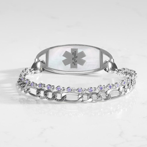 Silver women’s medical ID bracelet with white mother-of-pearl inlay tag and dual-chain design featuring violet crystal accents, displayed on a marble surface.