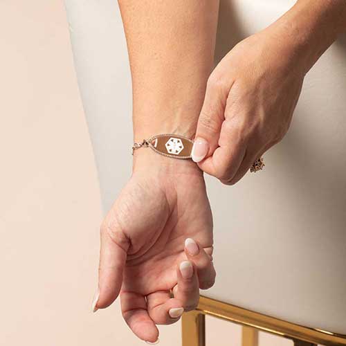 Close-up of a woman adjusting a rose gold medical ID tag featuring the medical alert symbol, blending safety and boutique style.