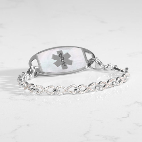 Silver medical ID bracelet showcasing a white mother-of-pearl tag with silver caduceus symbol, connected to a silver crystal-studded infinity-link chain.