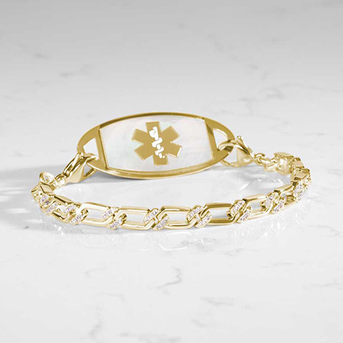 Stylish gold medical ID bracelet with clear mother-of-pearl inlay on the tag and CZ-accented chain links, displayed on a marble surface.