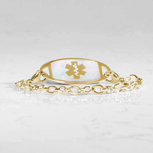 Gold medical ID bracelet with crystal-accented oval links and a white mother-of-pearl inlay on the ID tag, engraved with the gold medical caduceus symbol.