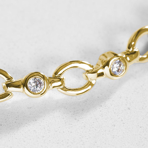 Close-up of gold oval chain links with bezel-set clear crystals, showcasing the polished finish and fine detailing.