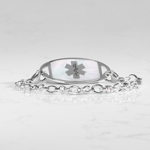 Silver Jovie medical ID bracelet featuring a white mother-of-pearl inlay tag with stainless medical symbol and crystal-accented oval links, shown on a white marble surface.