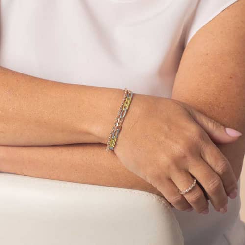 Woman wearing a mixed-metal medical ID bracelet strand featuring crystal accents and gold, silver, and rose gold chain links.