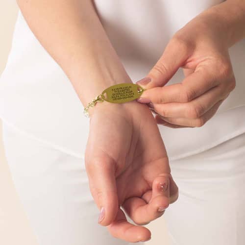 Woman displaying the engraved back of a gold medical ID bracelet with personalized medical information for emergency identification.