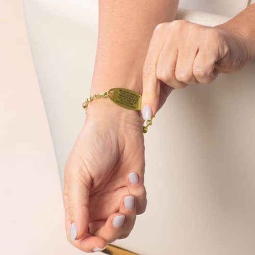 Model displaying the engraved back of a medical ID tag paired with the Mia Gold bracelet for personalized medical information.